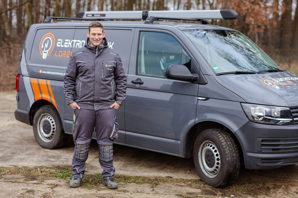Ihr Ansprechpartner bei Elektrotechnik Lorenz in Coesfeld Mitarbeiter von Elektrotechnik Lorenz steht vor einem Firmenfahrzeug mit Logo in herbstlicher Umgebung