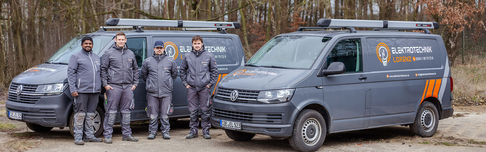 Team von Elektrotechnik Lorenz vor den Firmenfahrzeugen in Coesfeld Vier Mitarbeiter von Elektrotechnik Lorenz stehen in Arbeitskleidung vor zwei grauen VW-Transportern mit Firmenlogo auf einem Parkplatz