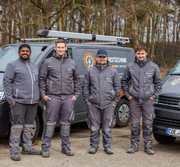 Elektro Coesfeld – Ihr Elektriker-Team im Münsterland Vier Elektriker von Elektrotechnik Lorenz in Coesfeld stehen in Arbeitskleidung vor den Firmenfahrzeugen im Münsterland