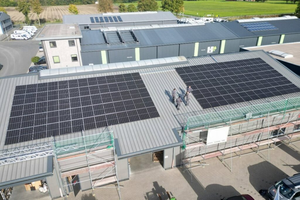 Solaranlage in Coesfeld – Montage auf einem Gewerbe-Flachdach Solaranlage in Coesfeld – Elektriker montieren Solarmodule auf dem Flachdach eines Gebäudes in der Vogelperspektive